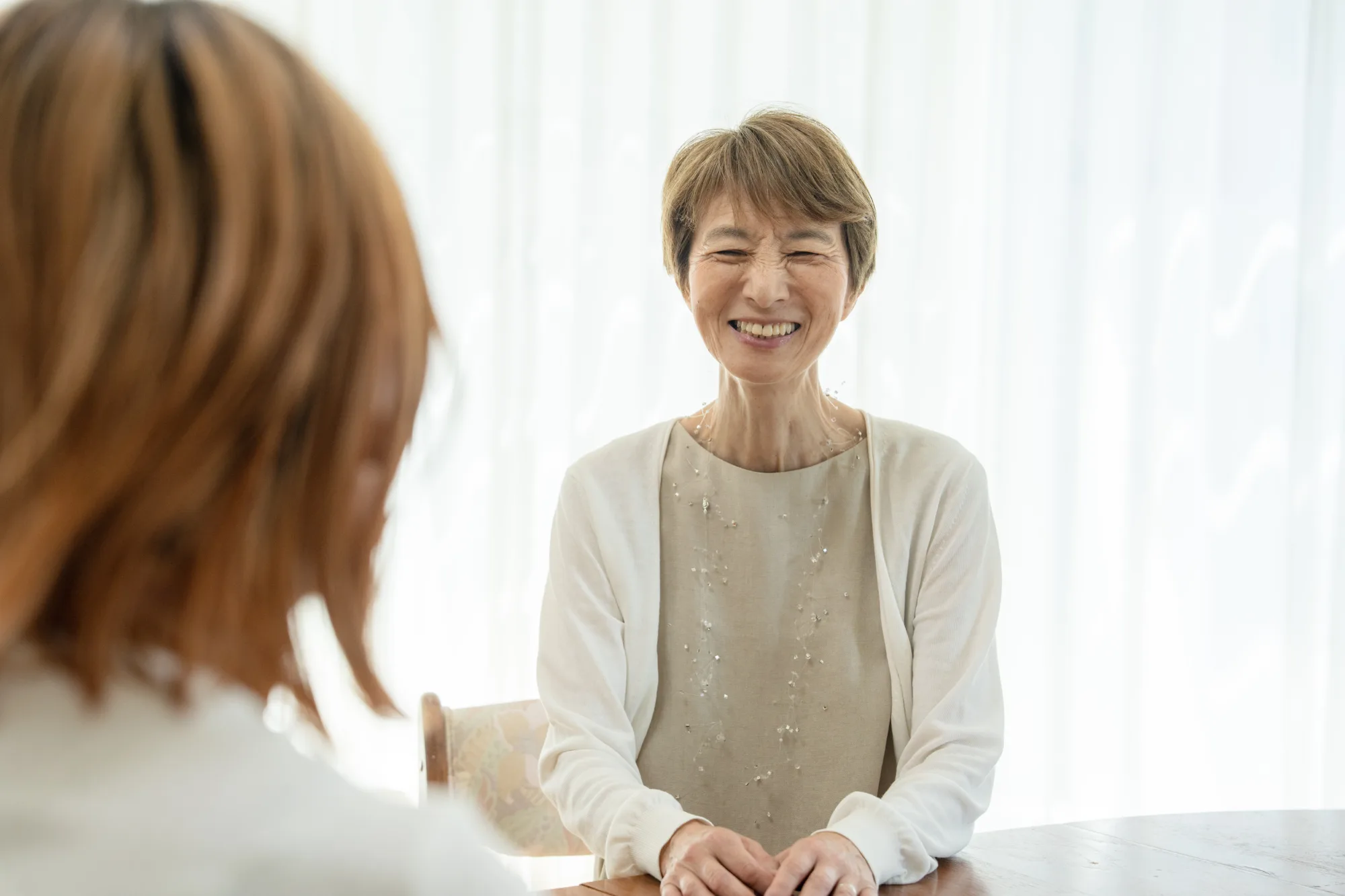 明るい部屋のテーブルで、穏やかに微笑みながら話を聞く女性