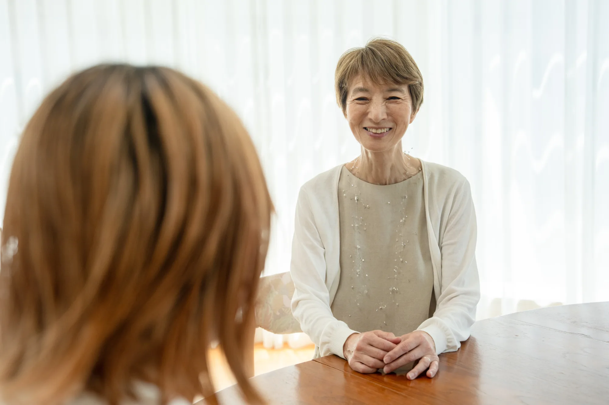 明るい部屋のテーブルで、穏やかに微笑みながら話を聞く女性