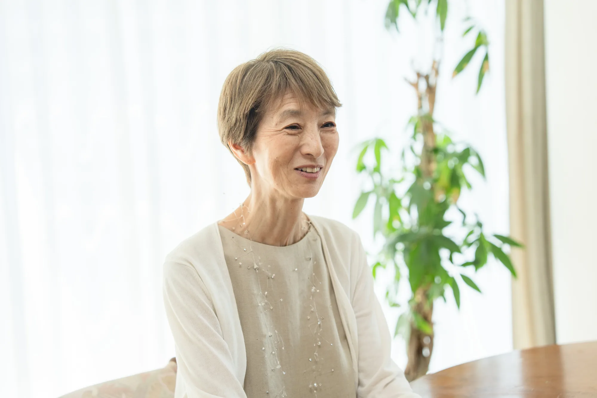 明るい部屋のテーブルで、穏やかに微笑みながら話を聞く女性