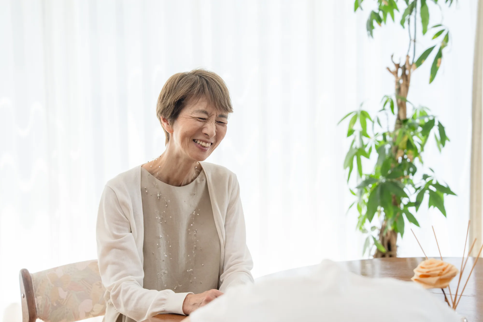 明るい部屋のテーブルで、穏やかに微笑みながら話を聞く女性
